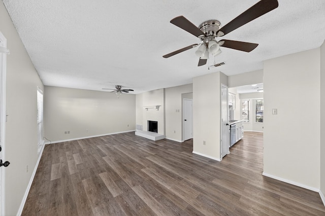 3208 Preston Dr, Midland, TX 79707 - unfurnished living room featuring ceiling fan, dark wood-style floors, a large fireplace, and a textured ceiling