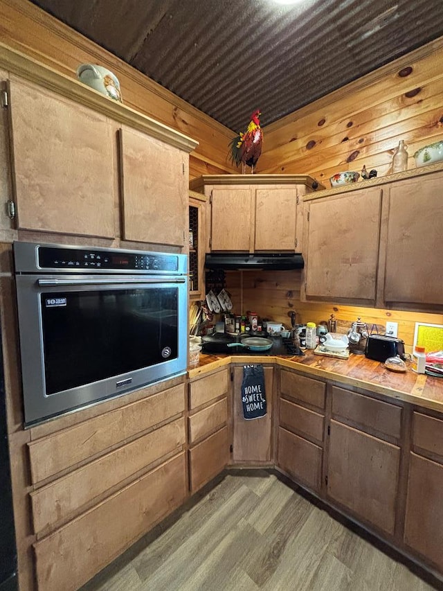 kitchen featuring light wood-type flooring, wood walls, under cabinet range hood, and oven