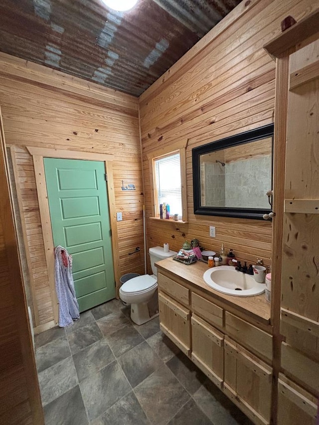 bathroom with toilet, wooden walls, stone finish floor, and vanity