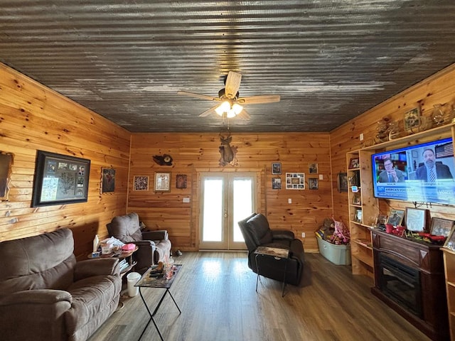 living room featuring wood finished floors, a ceiling fan, wood walls, and french doors
