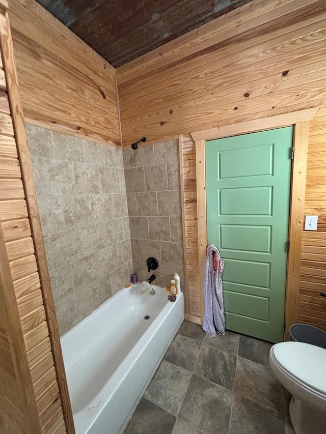 full bathroom featuring shower / bathtub combination, toilet, wooden walls, stone finish floor, and wood ceiling