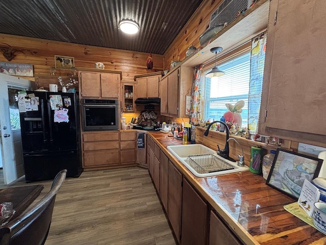 kitchen with wood finished floors, oven, a sink, wooden walls, and black fridge