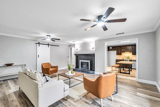 living area featuring a barn door, a ceiling fan, visible vents, light wood finished floors, and crown molding