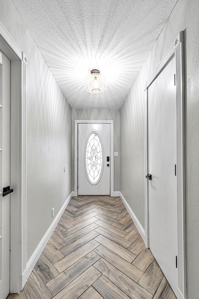 doorway to outside with baseboards, a textured ceiling, and a textured wall