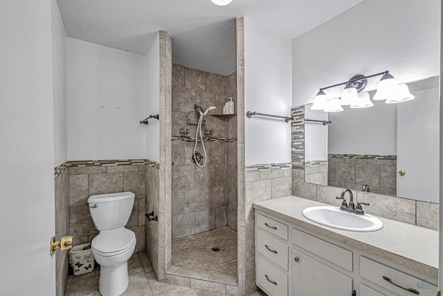 bathroom featuring tiled shower, vanity, toilet, and tile walls