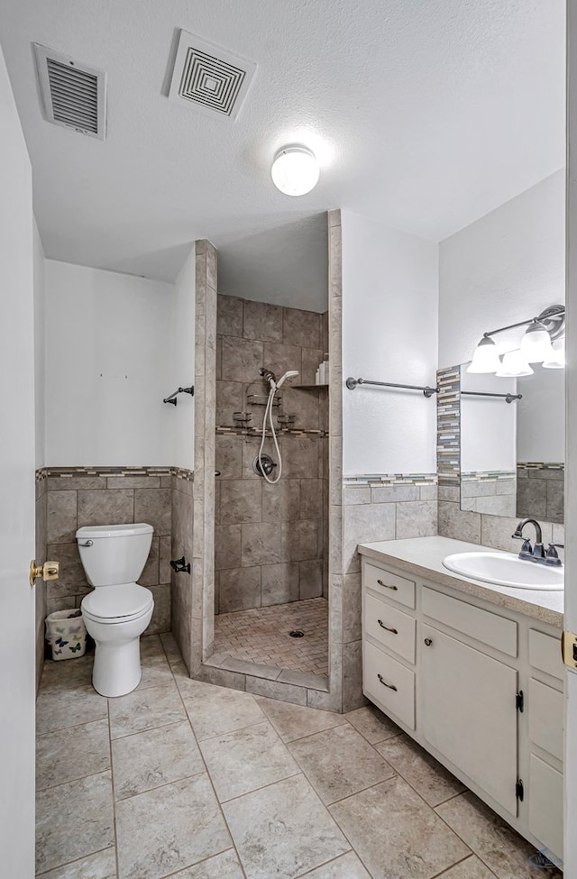 bathroom with vanity, tiled shower, tile walls, and a textured ceiling