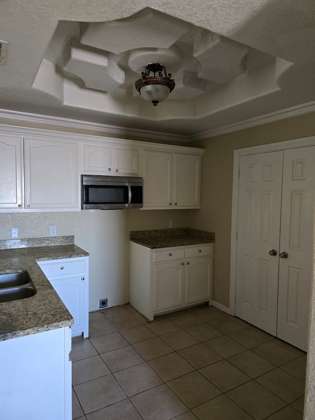 kitchen with light tile patterned floors, white cabinetry, crown molding, and a raised ceiling