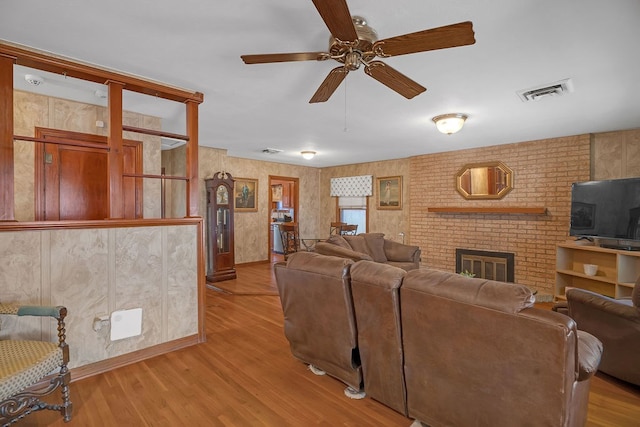 living area with a ceiling fan, visible vents, wood finished floors, and a fireplace