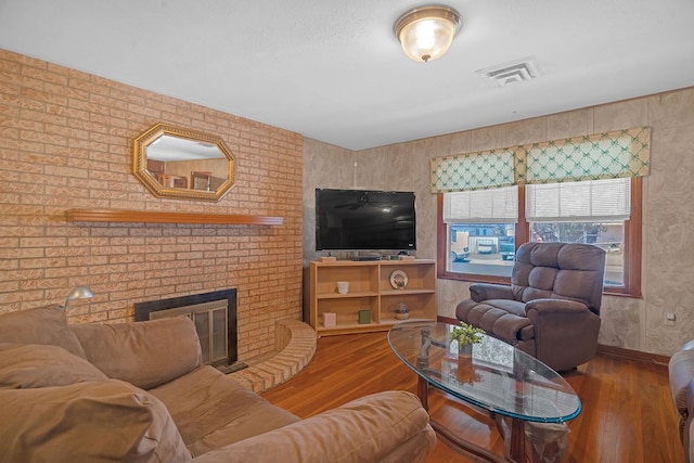 living room with a brick fireplace, baseboards, visible vents, and wood finished floors