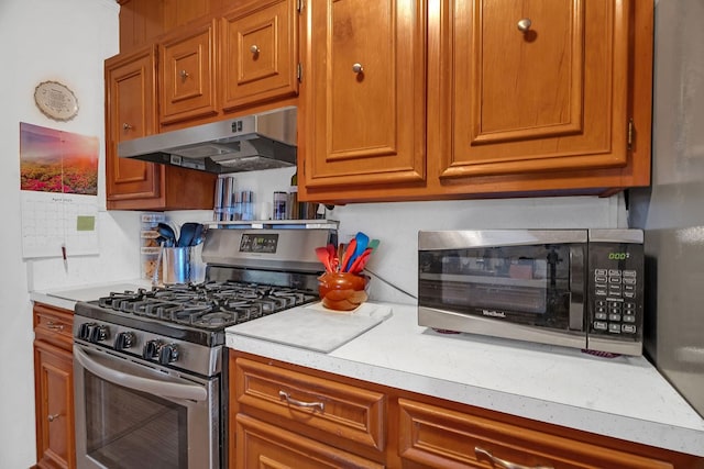 kitchen with under cabinet range hood, stainless steel appliances, brown cabinetry, and light countertops