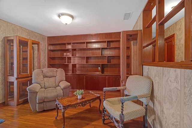 living area featuring wallpapered walls, visible vents, and wood finished floors