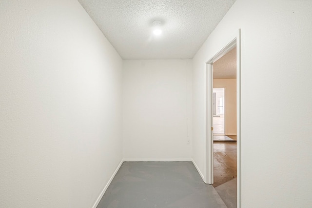 hall featuring concrete floors, baseboards, and a textured ceiling