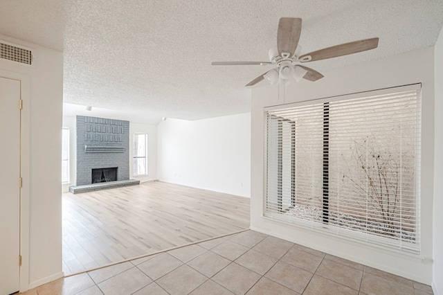 unfurnished living room featuring a fireplace, light tile patterned floors, visible vents, ceiling fan, and a textured ceiling