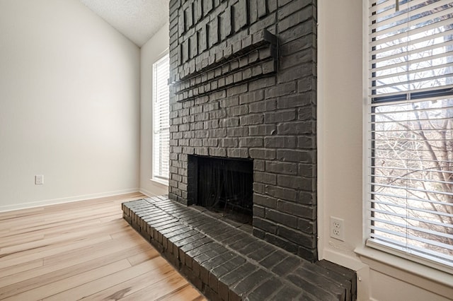 living room featuring lofted ceiling, light wood-style floors, a brick fireplace, a textured ceiling, and baseboards