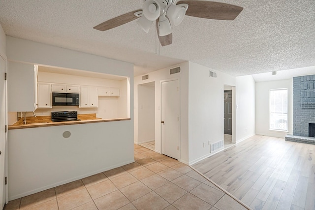 kitchen with visible vents, a peninsula, a fireplace, black microwave, and range with electric stovetop