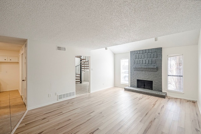 unfurnished living room featuring light wood-style floors, visible vents, a fireplace, and stairs