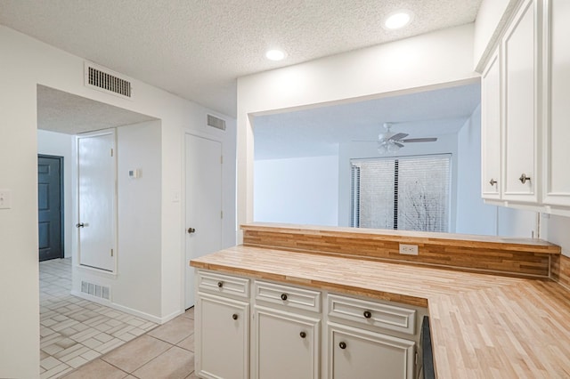 kitchen featuring visible vents, wooden counters, a textured ceiling, and white cabinetry