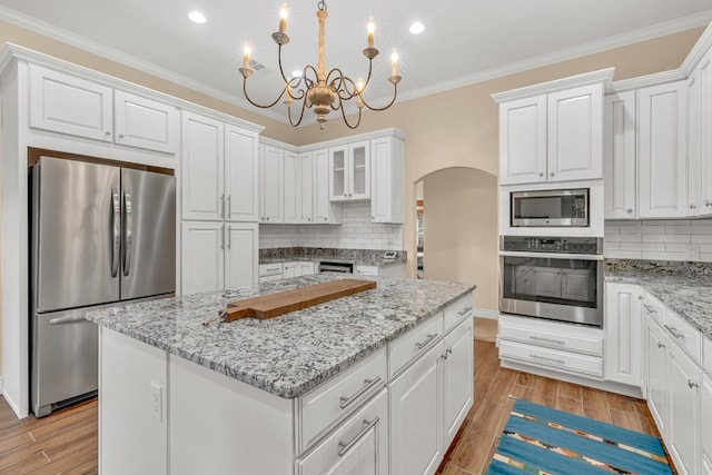 131 High Lonesome Dr, Alpine, TX 79830 - kitchen featuring appliances with stainless steel finishes, arched walkways, a kitchen island, white cabinets, and decorative backsplash