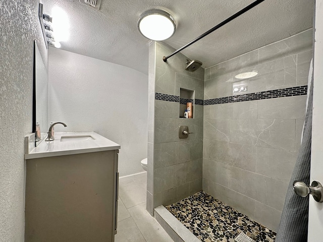 bathroom featuring vanity, tile patterned flooring, toilet, a textured ceiling, and a tile shower