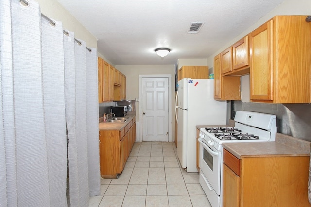 kitchen featuring sink, light tile patterned floors, white appliances, and a textured ceiling