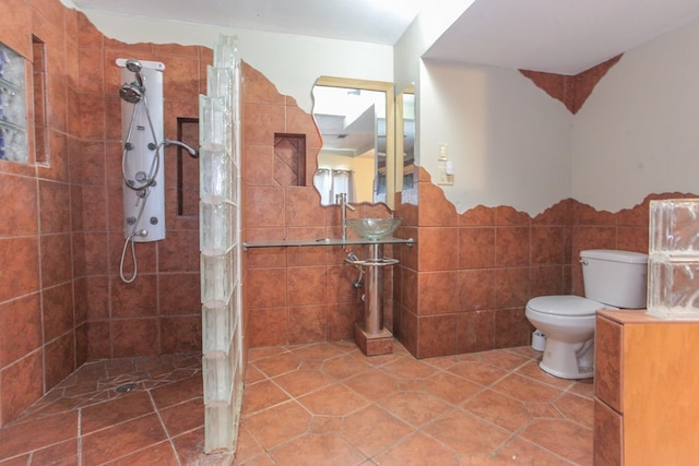 bathroom with a tile shower, tile walls, and toilet