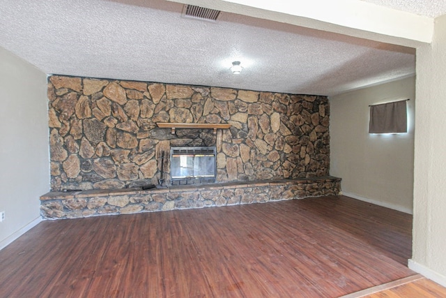 unfurnished living room with a textured ceiling, hardwood / wood-style flooring, and a stone fireplace