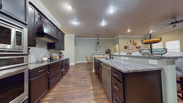 kitchen with stainless steel appliances, custom exhaust hood, a center island with sink, and pendant lighting