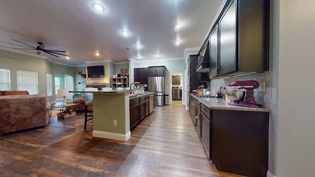 kitchen featuring a center island with sink, arched walkways, open floor plan, light stone countertops, and a kitchen bar