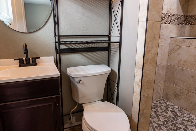 bathroom with a textured wall, tiled shower, vanity, and toilet