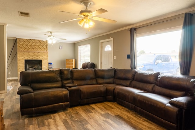 living area with visible vents, wood finished floors, a textured ceiling, crown molding, and a brick fireplace