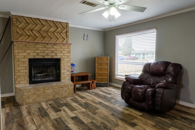 living area with wood finished floors, visible vents, baseboards, ornamental molding, and a brick fireplace