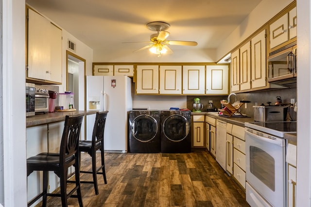 kitchen featuring white appliances, visible vents, washer and dryer, dark countertops, and dark wood finished floors