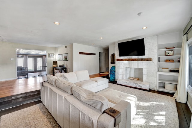 living area featuring built in features, recessed lighting, a stone fireplace, wood finished floors, and baseboards