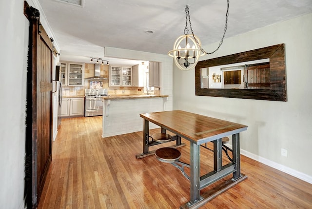 dining area featuring light wood finished floors, a barn door, baseboards, and track lighting