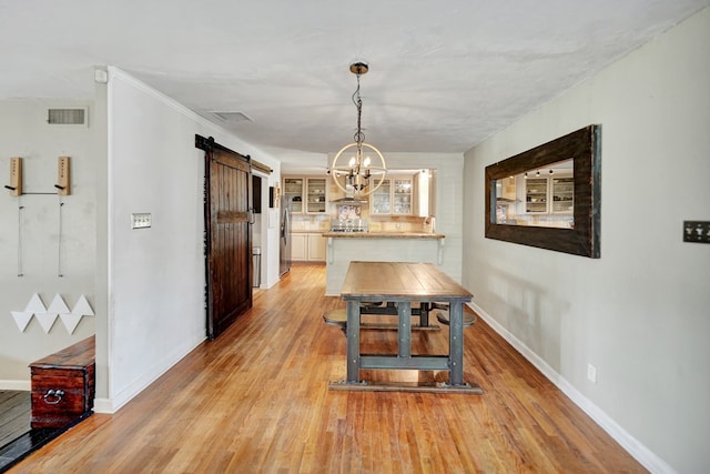 dining area with a barn door, visible vents, light wood-style flooring, and baseboards