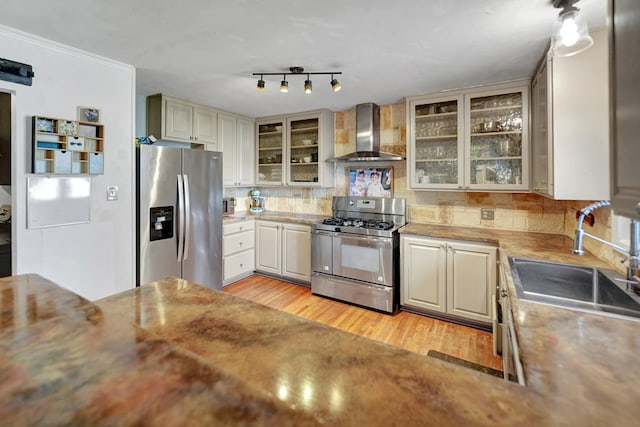 kitchen with tasteful backsplash, light wood-style floors, appliances with stainless steel finishes, wall chimney range hood, and a sink