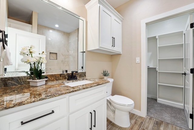 bathroom with tiled shower, hardwood / wood-style floors, vanity, and toilet