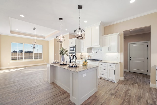 kitchen featuring light wood-type flooring, stainless steel appliances, decorative light fixtures, white cabinetry, and an island with sink