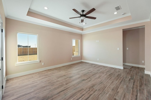 empty room featuring a tray ceiling, crown molding, and light hardwood / wood-style flooring