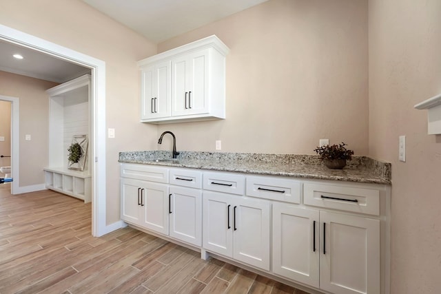 kitchen with light stone countertops, light hardwood / wood-style flooring, white cabinetry, and sink