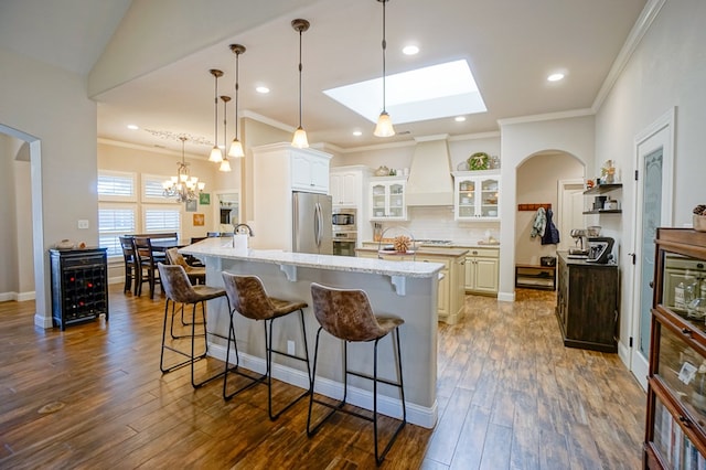 kitchen featuring arched walkways, glass insert cabinets, a kitchen breakfast bar, custom exhaust hood, and stainless steel appliances