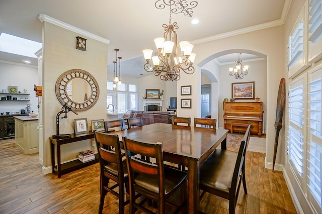 dining space with arched walkways, a fireplace, ornamental molding, wood finished floors, and baseboards