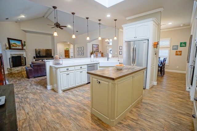 kitchen with arched walkways, butcher block counters, a sink, appliances with stainless steel finishes, and a center island