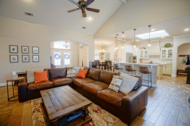 living area featuring high vaulted ceiling, arched walkways, visible vents, and wood finished floors