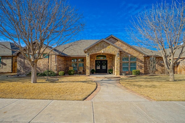 view of front of house featuring stone siding, french doors, a front yard, and brick siding