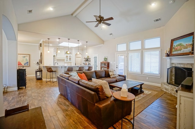 living room featuring high vaulted ceiling, wood-type flooring, a fireplace, and visible vents