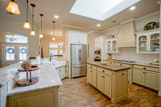 kitchen with custom range hood, a kitchen island, stainless steel appliances, french doors, and a sink