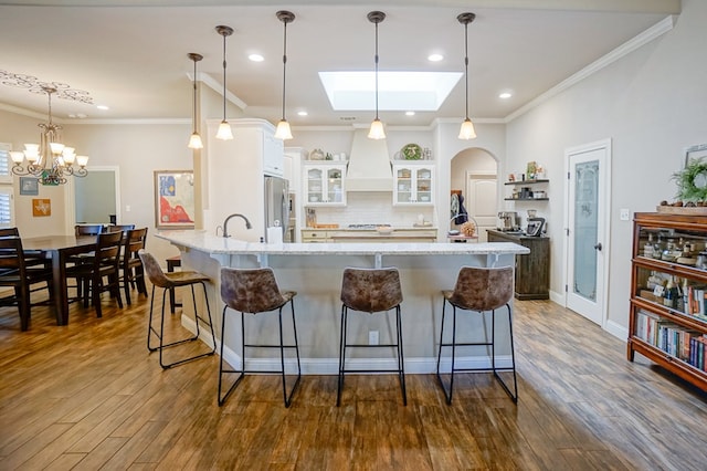 kitchen with custom exhaust hood, freestanding refrigerator, white cabinetry, a peninsula, and a kitchen breakfast bar