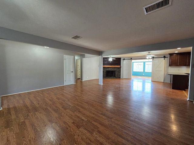 unfurnished living room featuring visible vents, a barn door, dark wood finished floors, and a fireplace