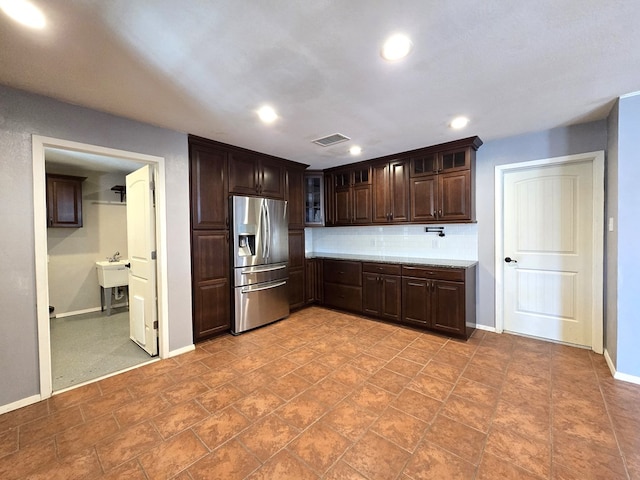 kitchen with dark brown cabinetry, decorative backsplash, glass insert cabinets, and stainless steel fridge with ice dispenser